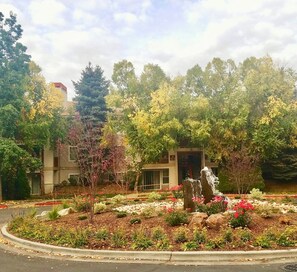 Un jardín ajardinado con una fuente, árboles y un edificio al fondo.