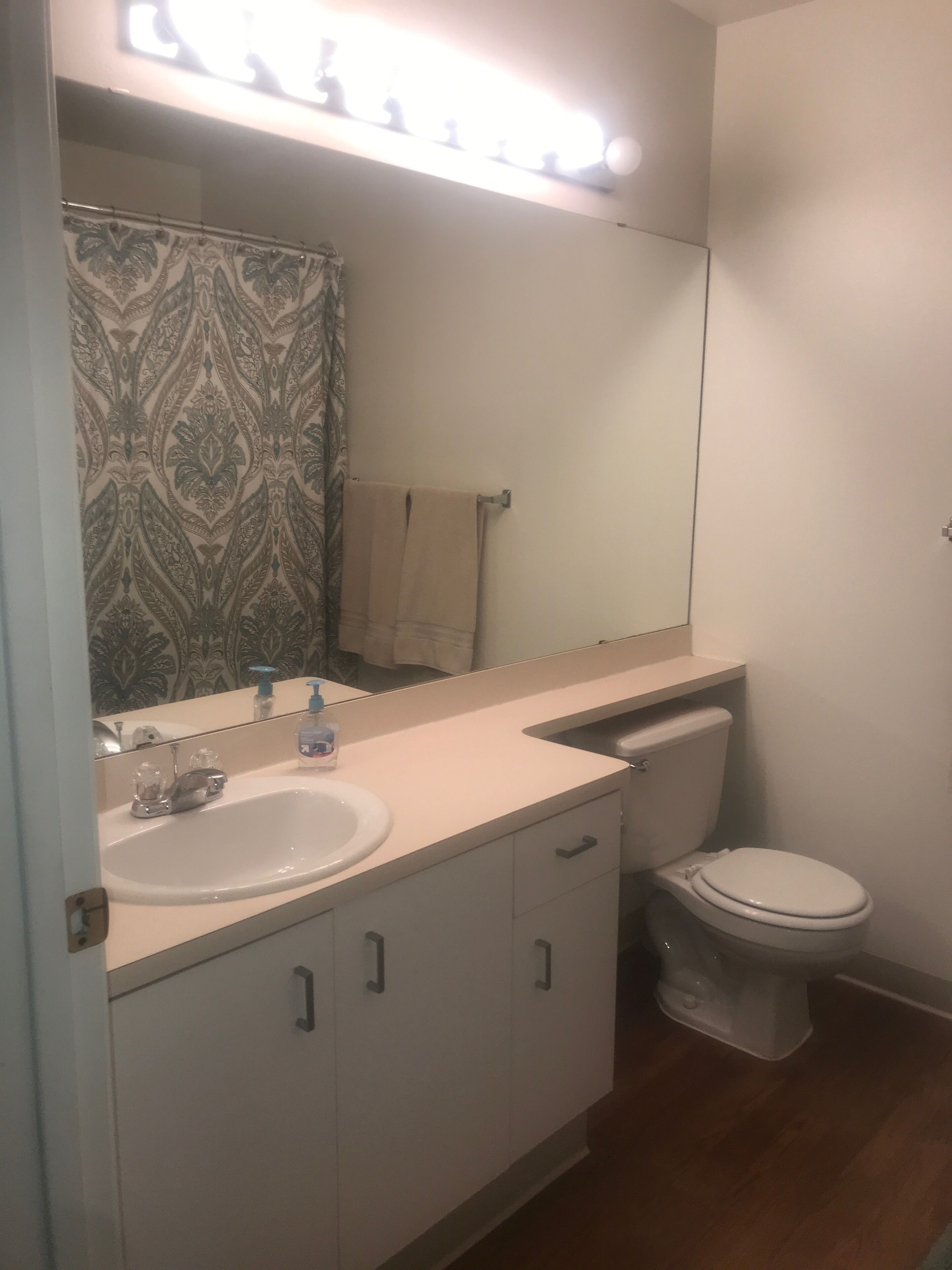 A bathroom with a white sink, mirror, and toilet. There is a patterned shower curtain and a towel hanging on the wall.