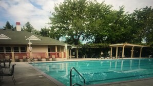 A swimming pool with a covered area, a building with a porch, and trees in the background.