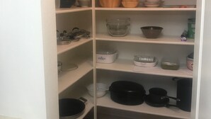 A kitchen pantry with shelves containing various kitchenware, including bowls, baking dishes, and pots.