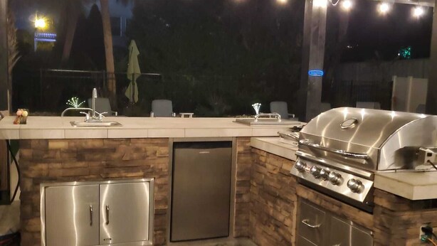 Ett utomhuskök med en inbyggd grill, en diskho och ett kylskåp.