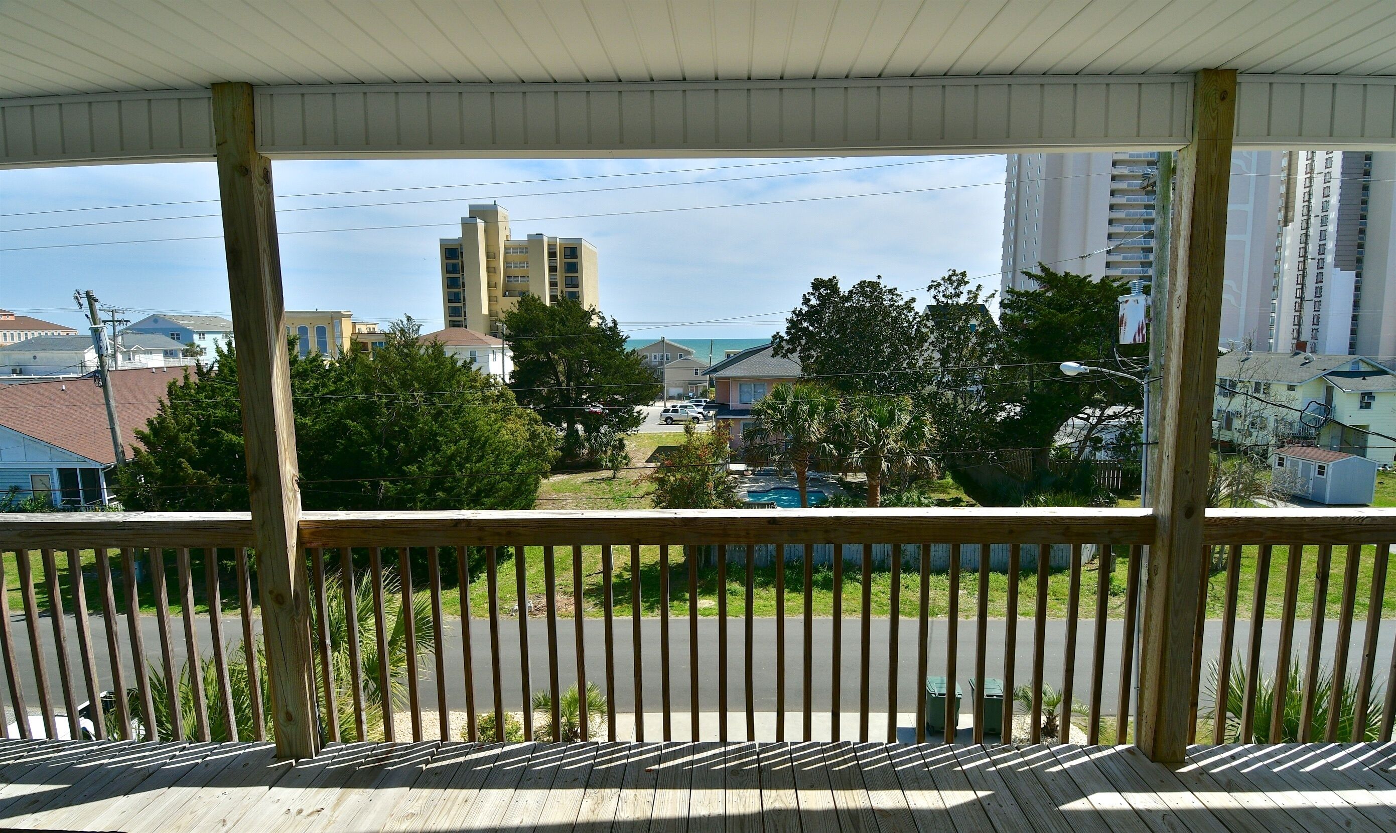 A wooden balcony with a view of a residential area, including houses and a tall building.