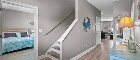 A modern interior with a staircase, a bed with patterned bedding, a blue wall decoration, and a table with a lamp.