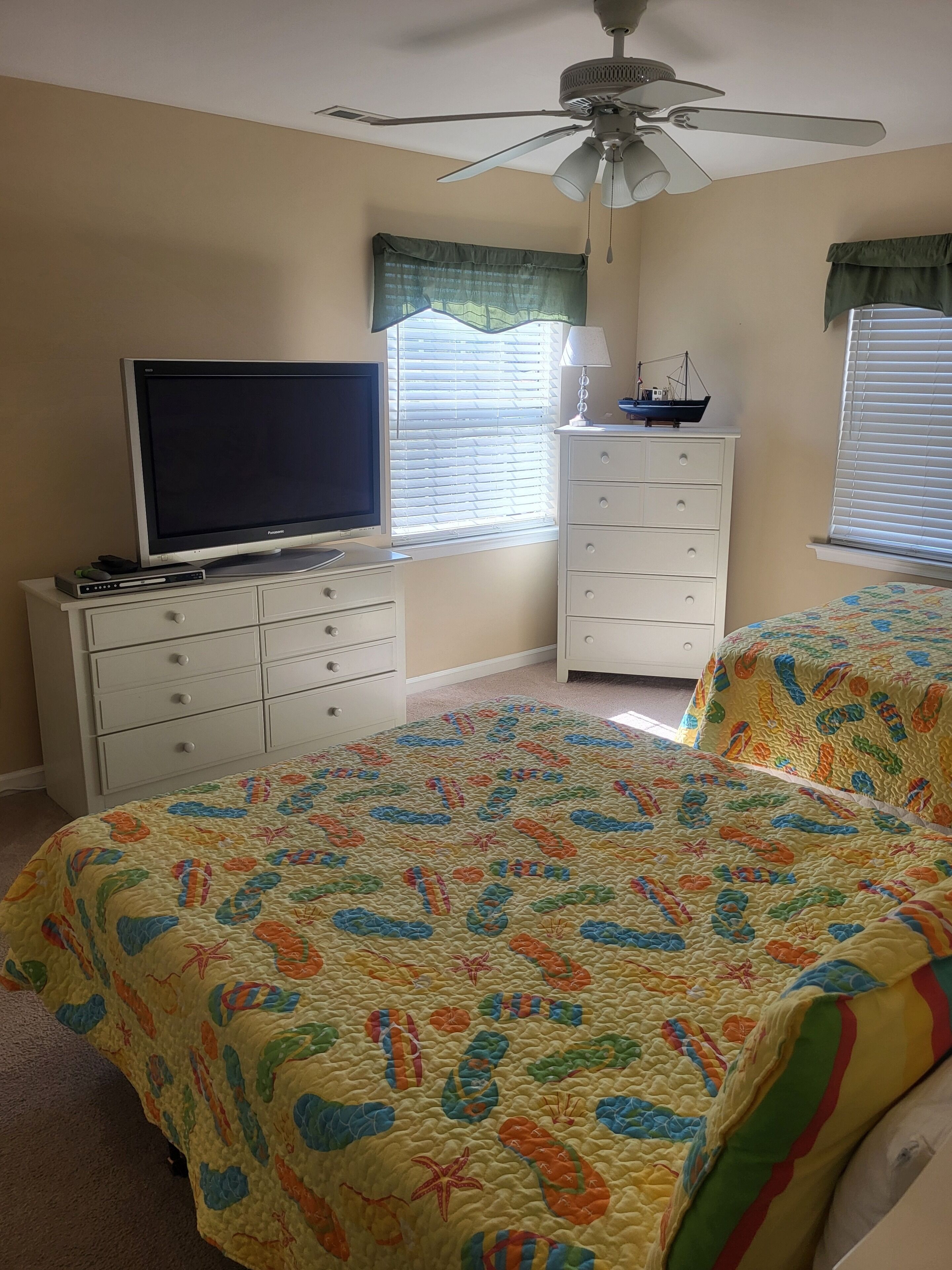Een slaapkamer met een bed, een dressoir, een televisie en een plafondventilator.