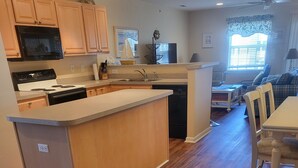A modern kitchen with wooden cabinets, a central island, and a dining area with a table and chairs. - 1206 Palms, 3-bedroom, 2-bath condo, Sept dates at last minute & off-season rate (Rehoboth Beach)