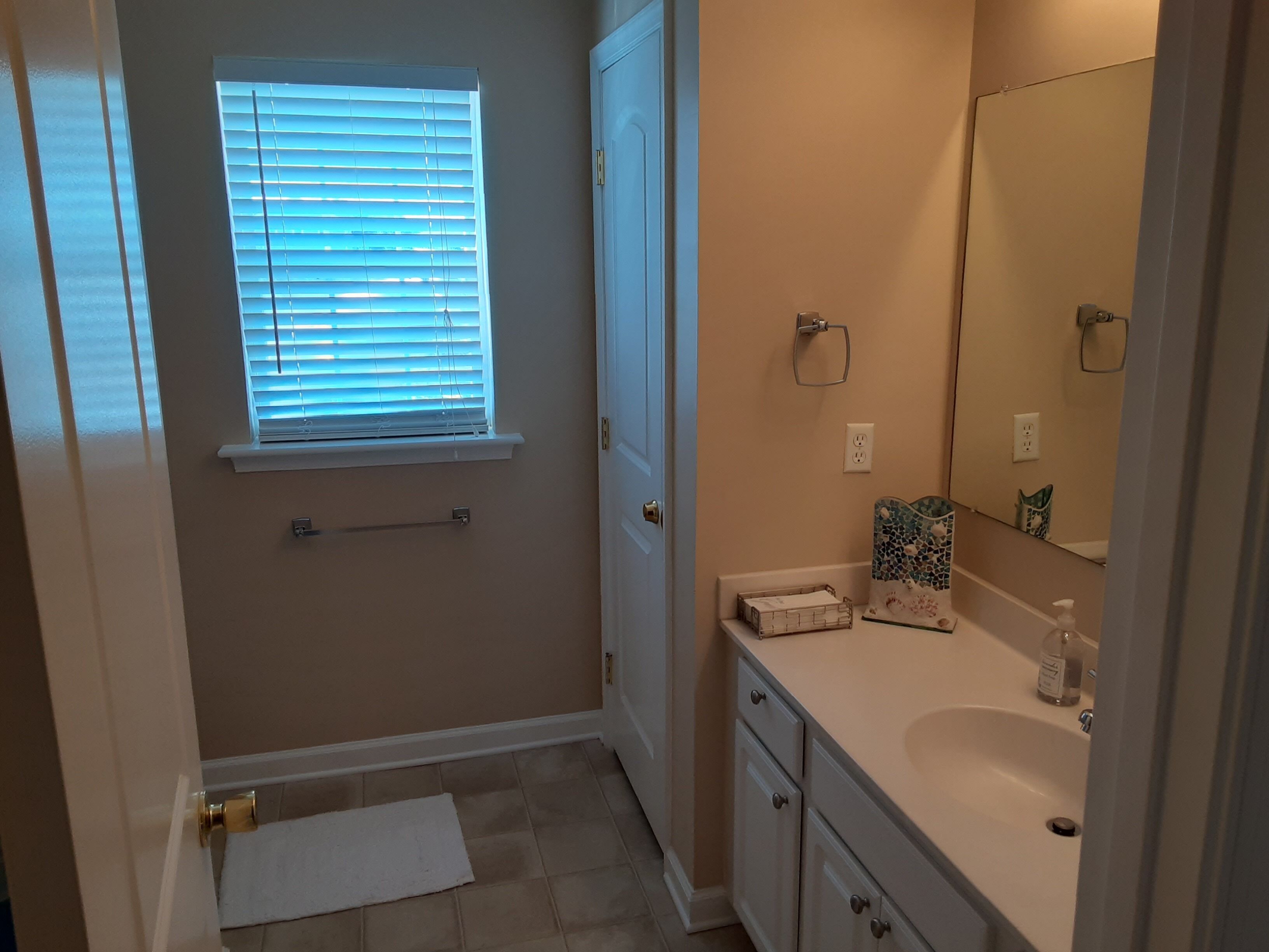 A bathroom with a white sink, a mirror, a towel rack, and a window with blinds.