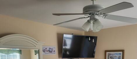Une chambre dotée d’un ventilateur de plafond, d’un téléviseur à écran plat, d’une commode et d’un lit recouvert d’une courtepointe à motifs marins.