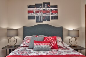 Un lit bien fait, avec une literie à motifs, deux tables de chevet avec des lampes et une œuvre d’art murale au-dessus du lit.