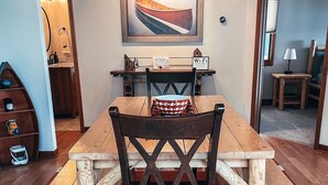 Un comedor con una mesa y sillas de madera, un cuadro sobre la mesa y una alfombra en el suelo.