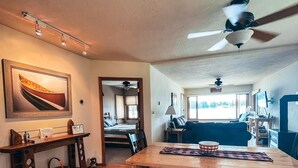 Un salón amplio con una mesa de madera, bancos, un ventilador de techo y un ventanal grande.