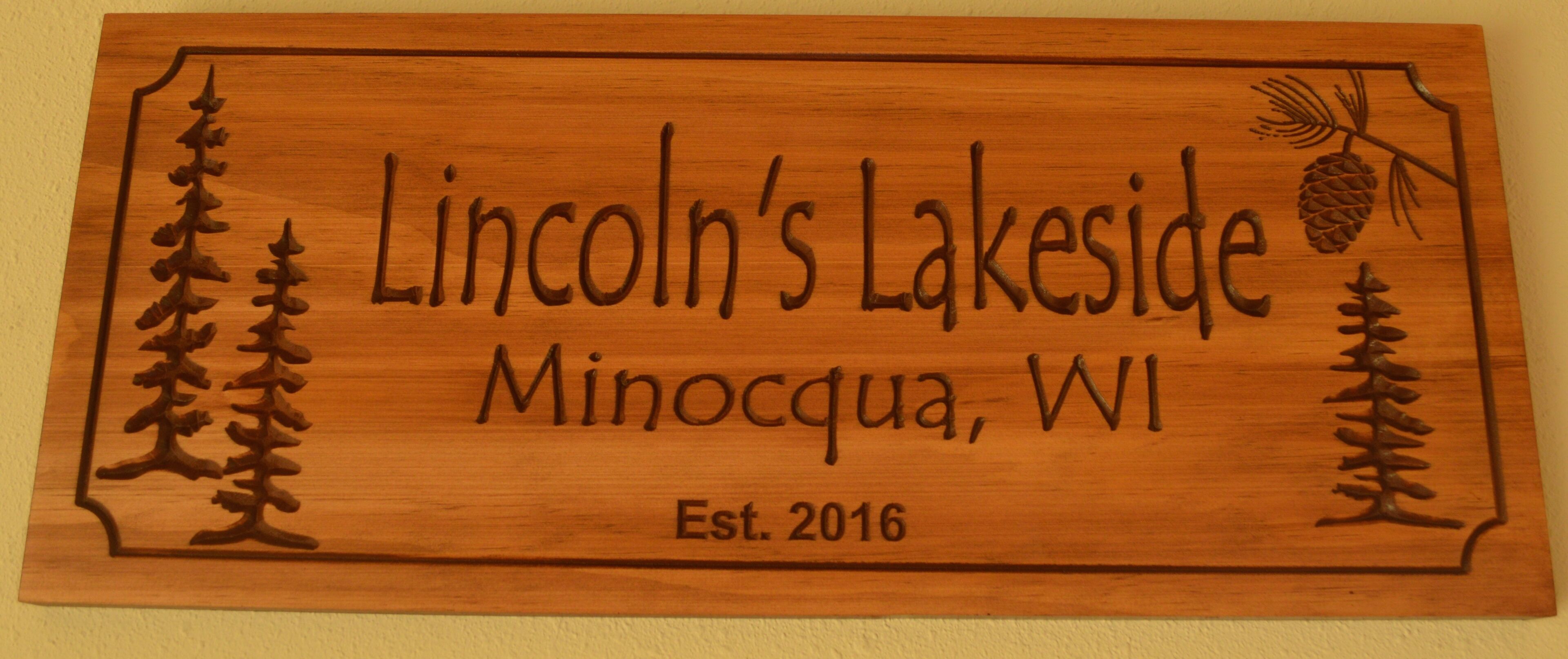 Un letrero de madera con árboles tallados y el texto que dice "Lincoln's Lakeside Minocqua, WI Est. 2016".
