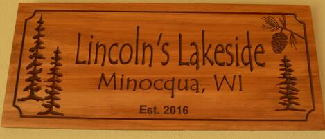 Un letrero de madera con árboles tallados y el texto que dice "Lincoln's Lakeside Minocqua, WI Est. 2016".