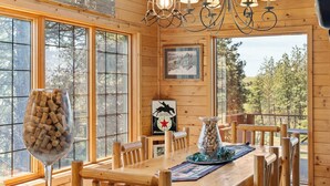 A wooden cabin interior with a dining table, chairs, a chandelier, and large windows offering a view of the outdoors. - Tranquil Country Lodge Getaway with Hot Tub!  Privacy & Serenity Abound... (Cheney)