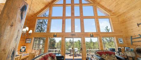 A log cabin interior with a large central window, wooden walls, a sofa, and a dining area.