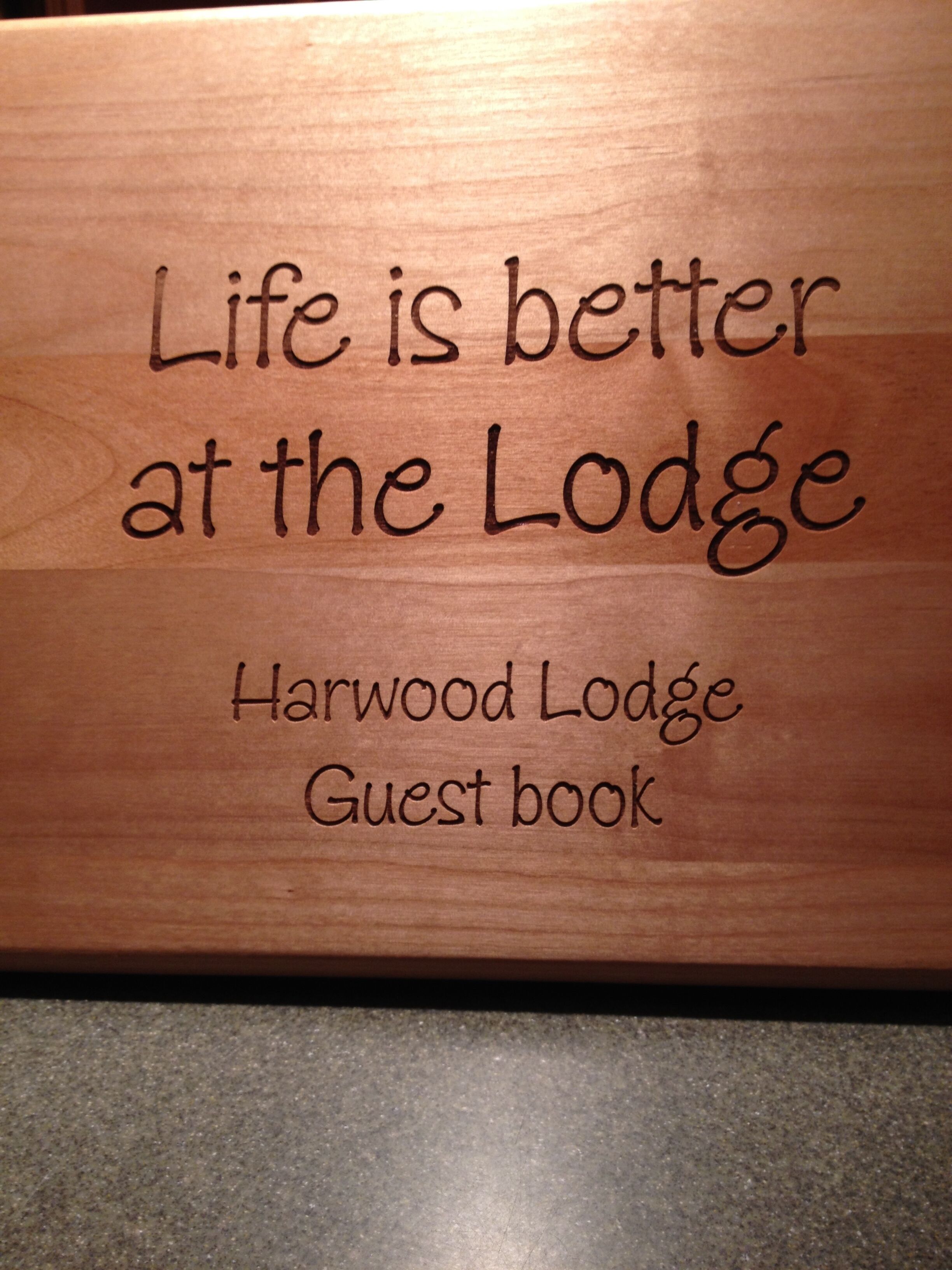A wooden plaque with the text 'Life is better at the Lodge' and 'Harwood Lodge Guest book'.