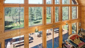 A spacious room with large windows offering a view of a forested area. There is a wooden ceiling and a chandelier. - Tranquil Country Lodge Getaway with Hot Tub!  Privacy & Serenity Abound... (Cheney)