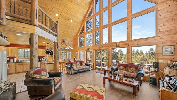 A spacious log cabin interior with a high ceiling, large windows, a dining area, and a cozy living room with leather sofas and a fireplace. - Tranquil Country Lodge Getaway with Hot Tub!  Privacy & Serenity Abound... (Cheney)