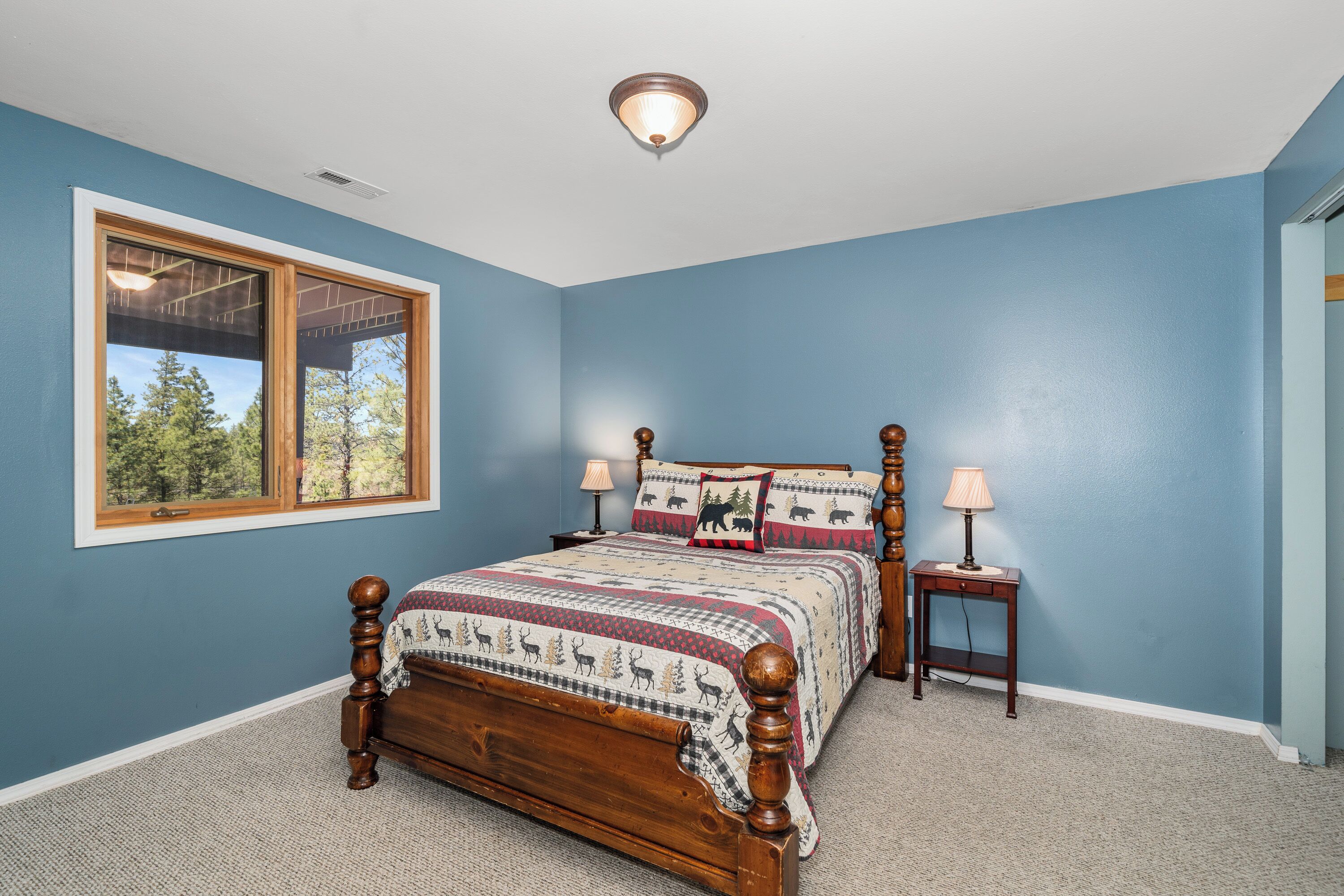 A bedroom with a large window, a wooden bed, two bedside tables with lamps, and a ceiling light fixture.
