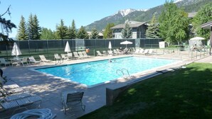 A swimming pool with lounge chairs and umbrellas, surrounded by a fence, with mountains in the background.