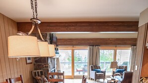 A dining area with a wooden table set for a meal, surrounded by chairs, and a view of the outdoors through large windows.