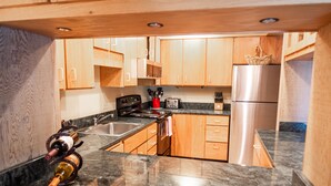 A modern kitchen with wooden cabinets, a stainless steel refrigerator, a granite countertop, and a wine bottle on the counter.