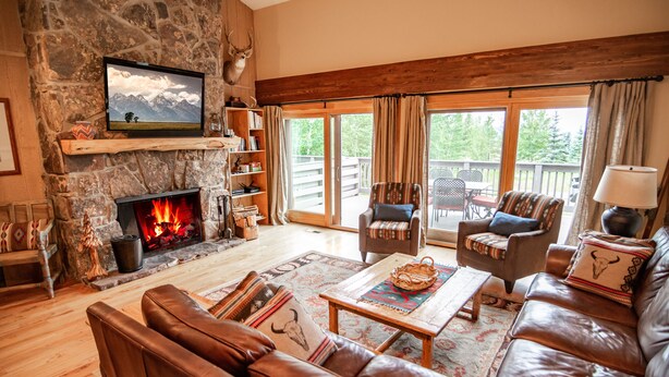 A cozy living room with a stone fireplace, leather sofas, and a large window overlooking a deck.