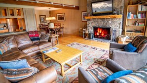 A cozy living room with a stone fireplace, leather sofas, a wooden coffee table, and a bookshelf.