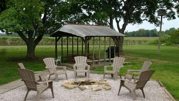 An outdoor seating area with Adirondack chairs and a fire pit, surrounded by a gravel area and a metal gazebo.