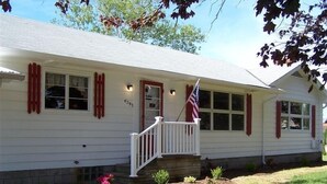 A single-story house with a white exterior, red shutters, and a small porch with a white railing.