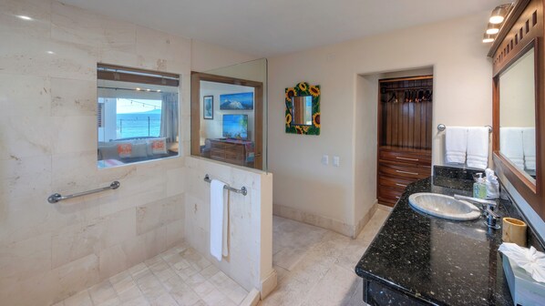 Un baño con pared de mármol, cabina de ducha de vidrio, lavamanos con encimera negra y tocador de madera.