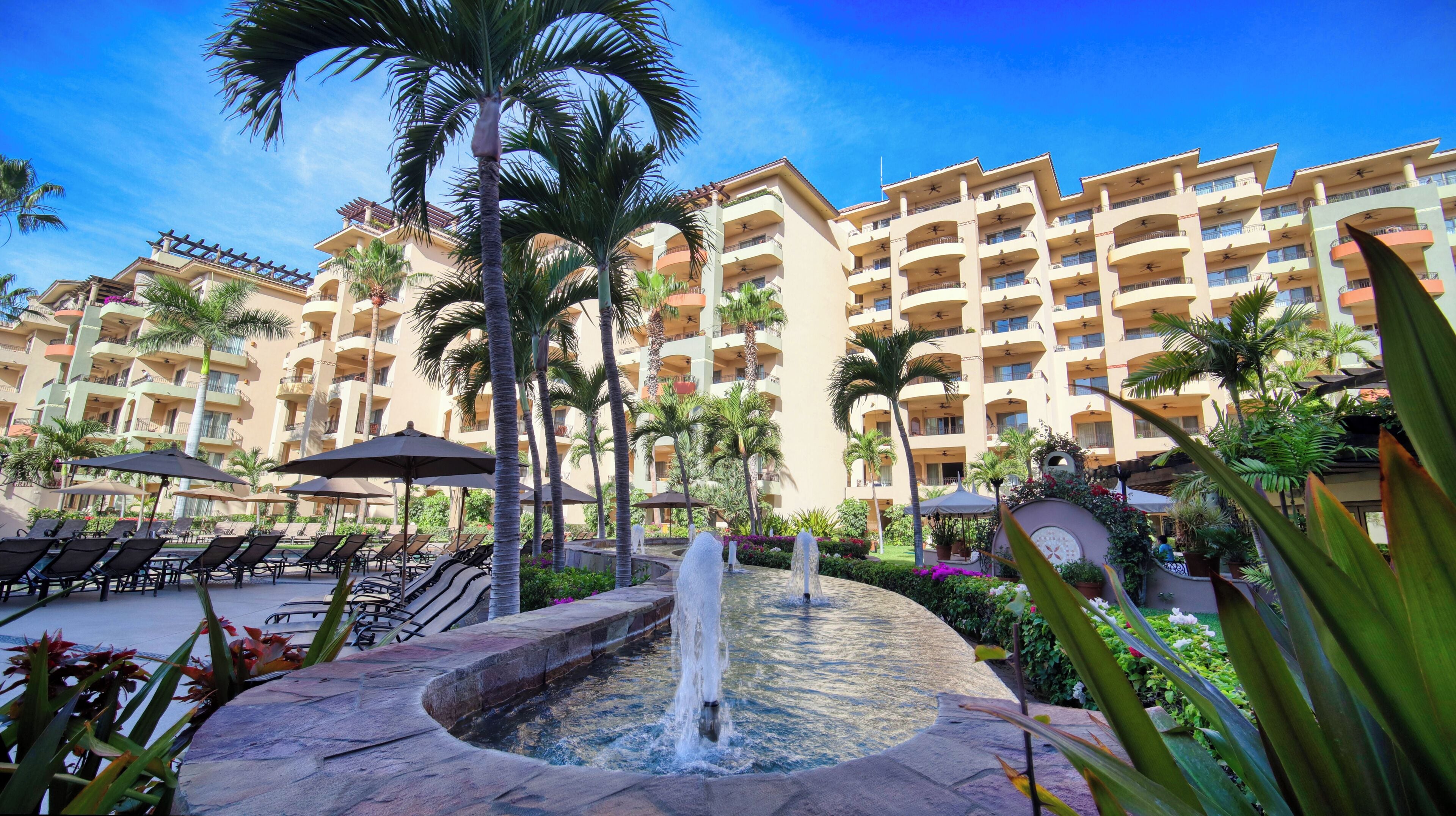 A hotel with multiple balconies, a pool area with lounge chairs, and a central water feature.