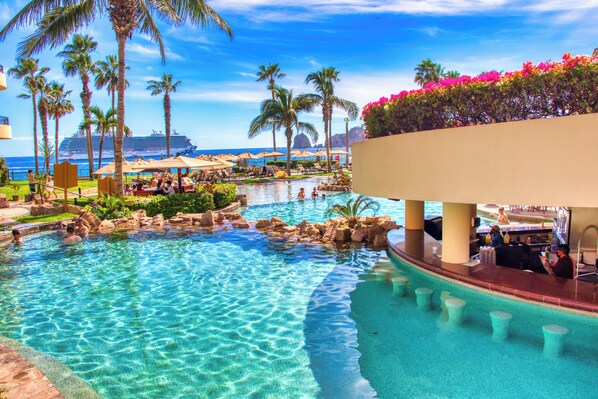 Ein Pool im Resort mit klarem Wasser, Palmen und Blick auf den Ozean.