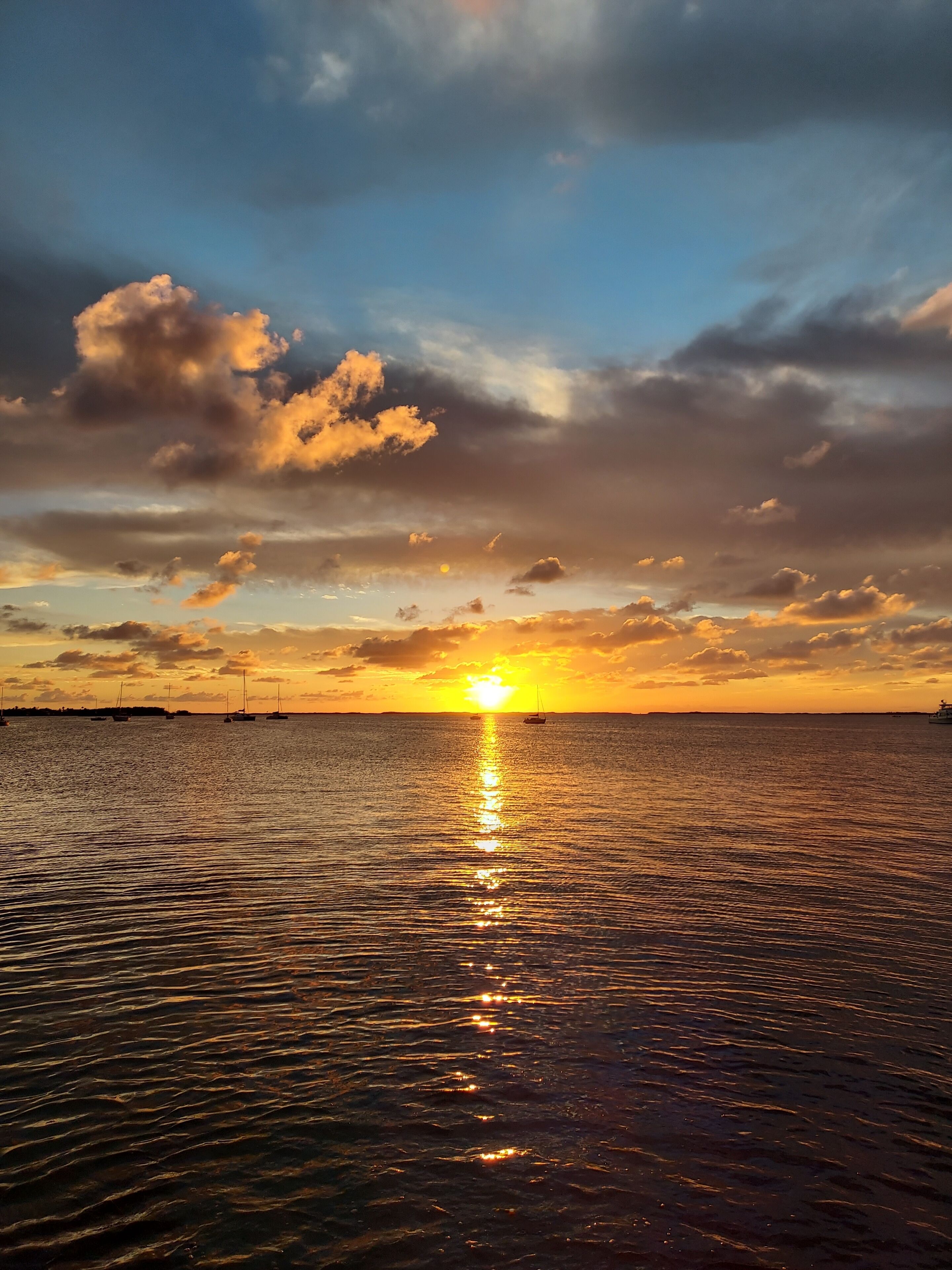 Un coucher de soleil sur une mer calme, avec des bateaux et un horizon dégagé.
