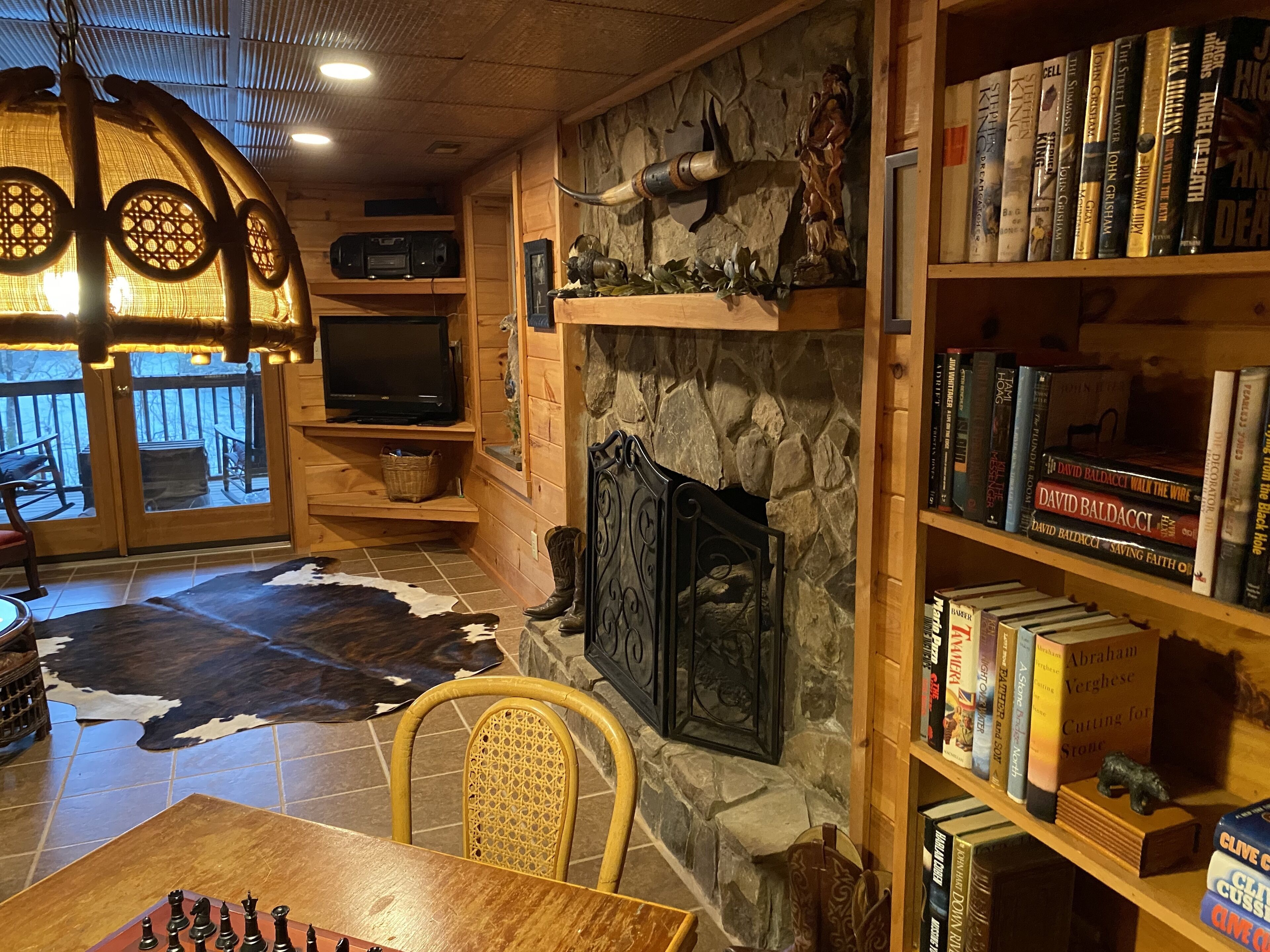 Una habitación acogedora con chimenea de piedra, una estantería llena de libros, un televisor y un tablero de ajedrez sobre una mesa de madera.