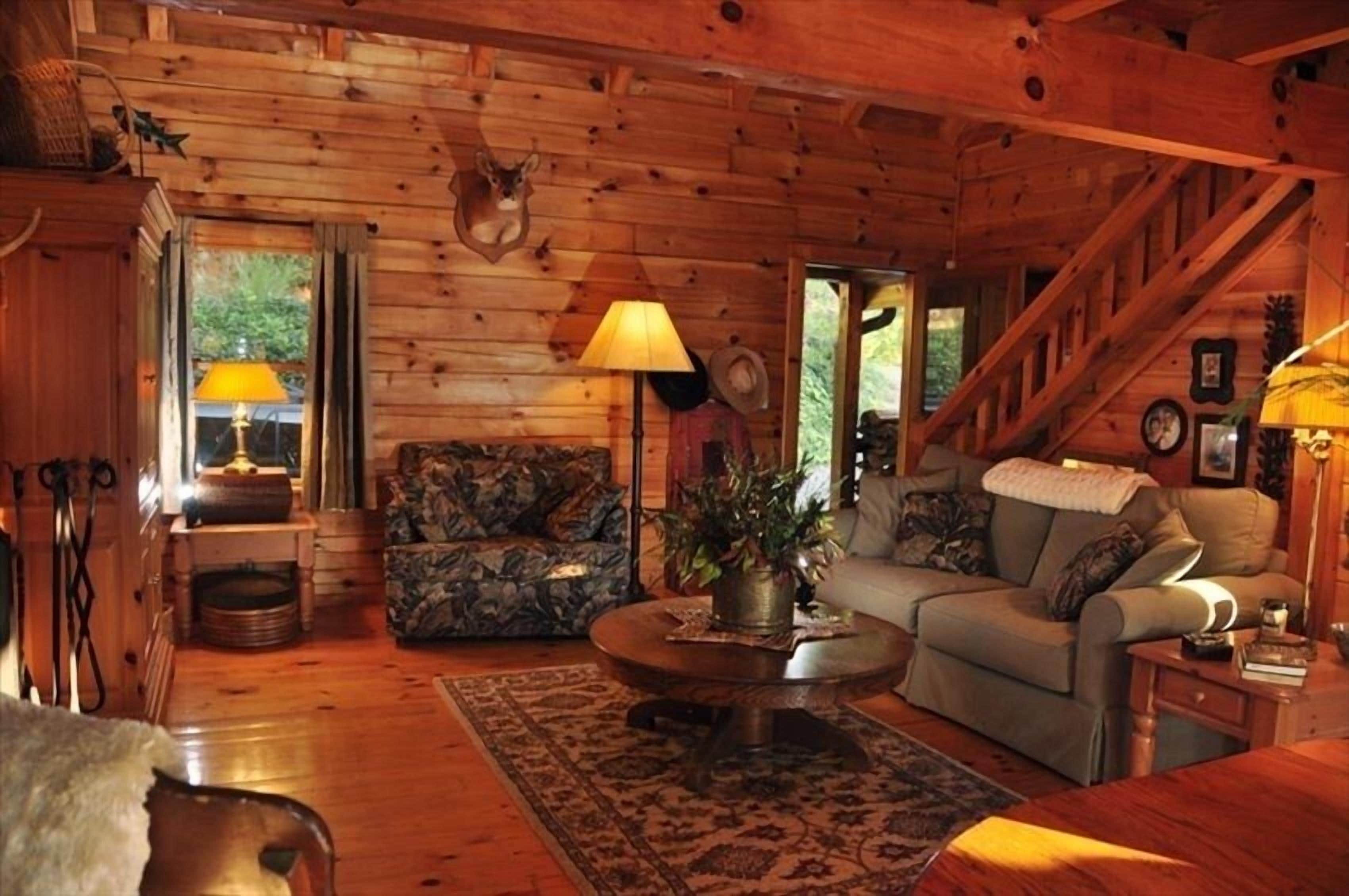 A cozy cabin interior with a wooden ceiling, a sofa, a coffee table, and a staircase.