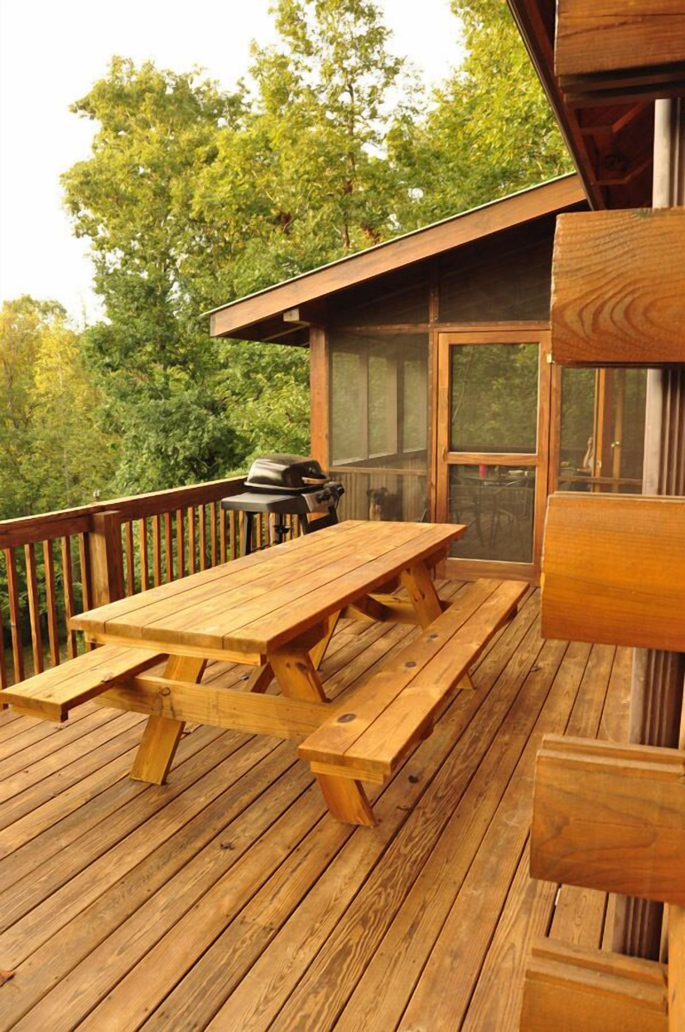 A wooden deck with picnic tables and a grill.