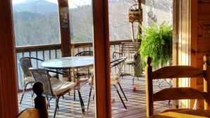 Eine Holzterrasse mit rundem Tisch und Stühlen, einem Deckenventilator und Blick auf Berge.
