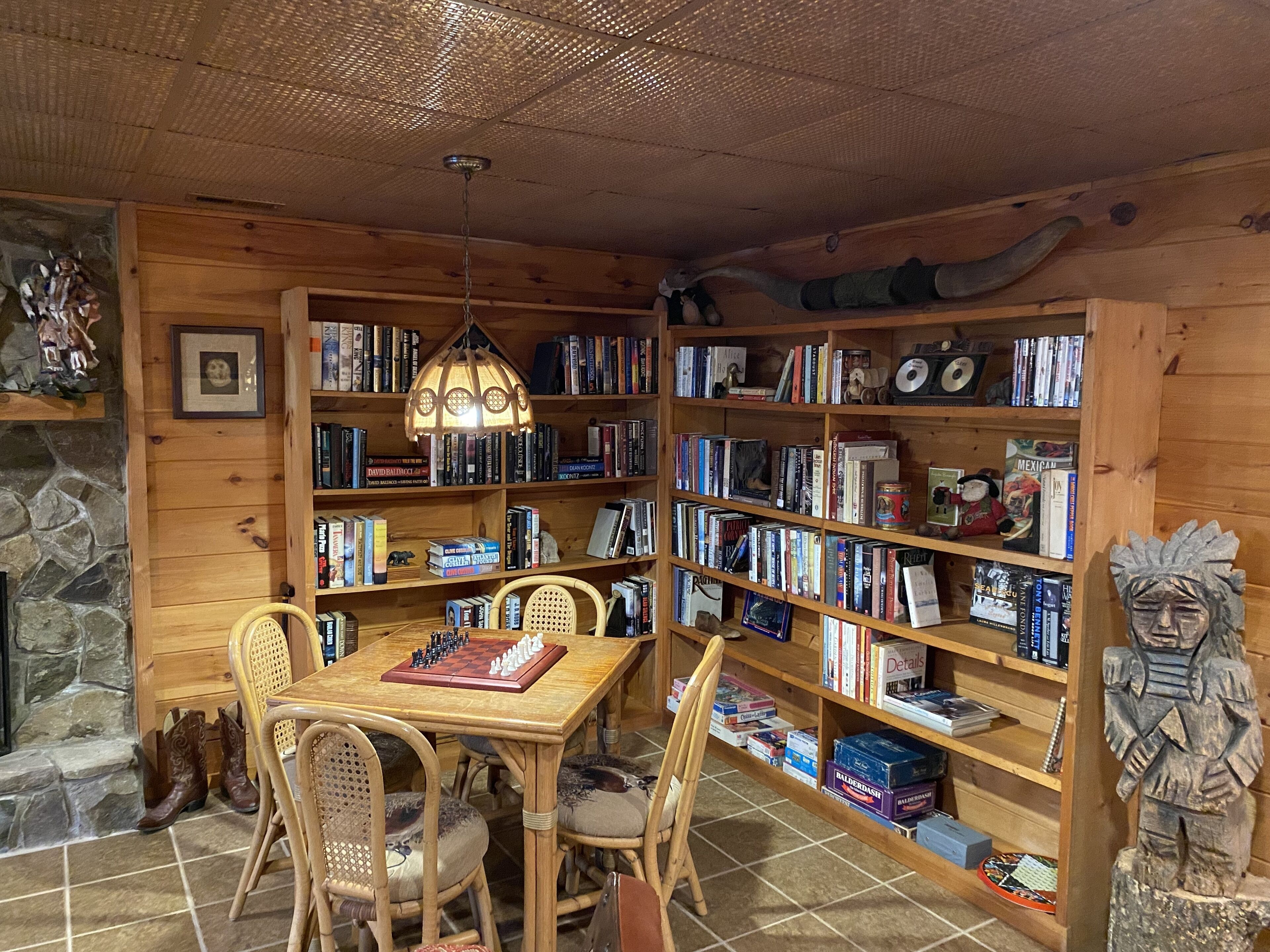 A cozy room with a wooden bookshelf filled with books, a wooden dining table with chairs, and a stone fireplace.