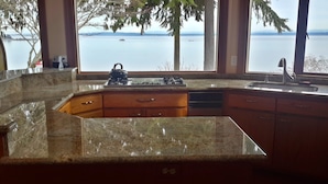 Une cuisine dotée de plans de travail en granit, de meubles en bois et offrant une vue sur un lac grâce à de grandes fenêtres.