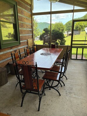 A wooden dining table with chairs, a window with a view of greenery, and a concrete floor. - Sugar Plum Cabin - Beautiful leaf & Mountain View, Kids Ski FREE, Holiday FUN (Maggie Valley)