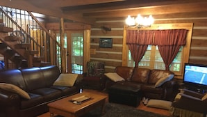A cozy log cabin interior with a leather sofa, a wooden coffee table, and a television.