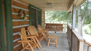 A wooden porch with four Adirondack chairs and a bench, a wooden door with a number, and a wreath on the wall.