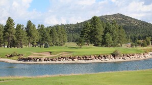 A golf course with a water body, trees, and a hill in the background.