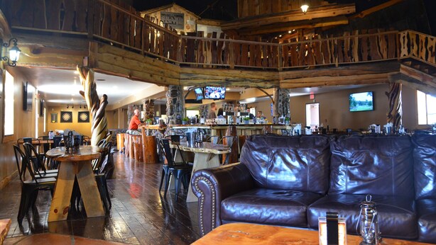 A multi-level bar area with wooden decor, leather seating, and a television screen.
