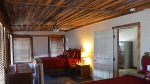 A bedroom with a wooden ceiling, a bed with red bedding, a bedside table with a lamp, and a wardrobe.