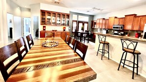 Un grand espace à manger avec une table et des chaises en bois, une cuisine dotée de meubles en bois et un ventilateur de plafond.