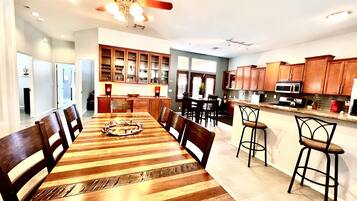 A spacious dining area with a wooden table and chairs, a kitchen with wooden cabinets, and a ceiling fan.
