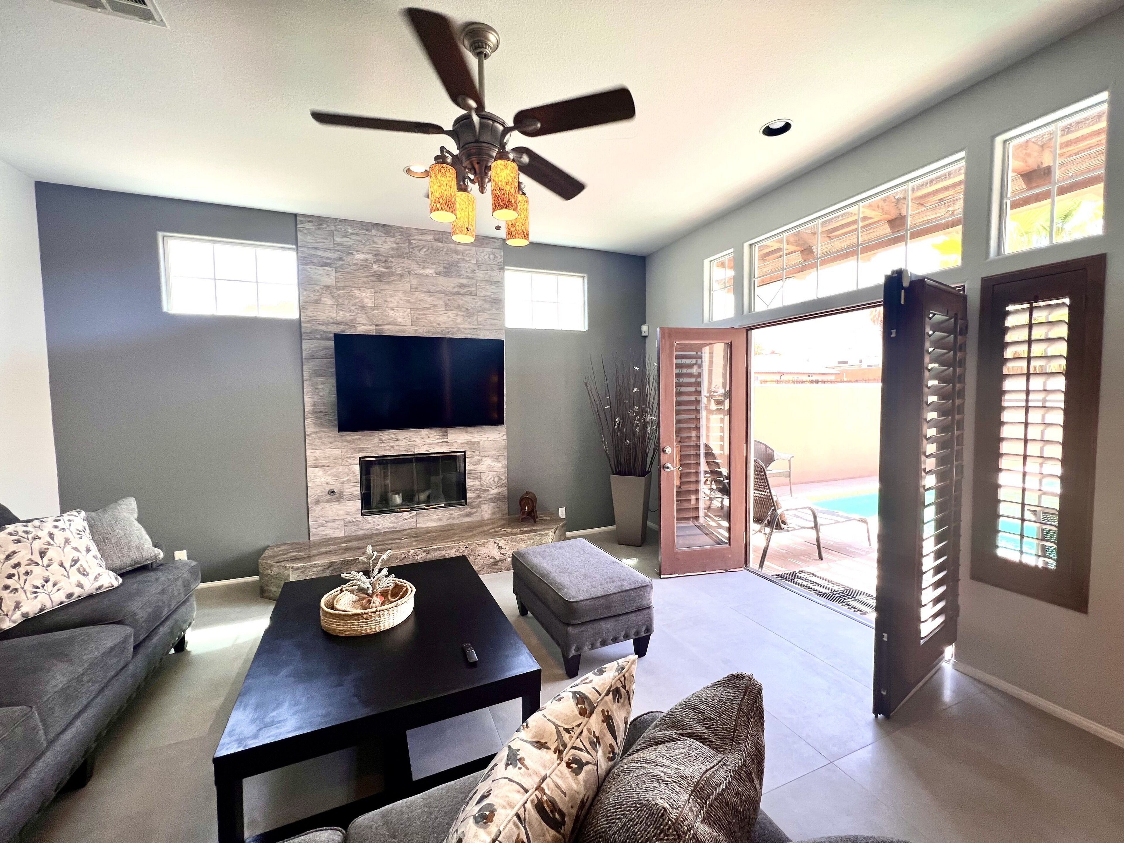 A living room with a fireplace, a ceiling fan, and a TV mounted on the wall.