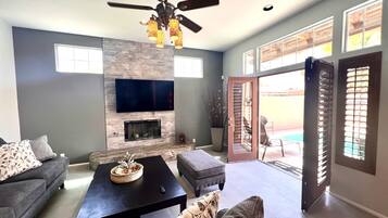 A living room with a fireplace, a ceiling fan, and a TV mounted on the wall.