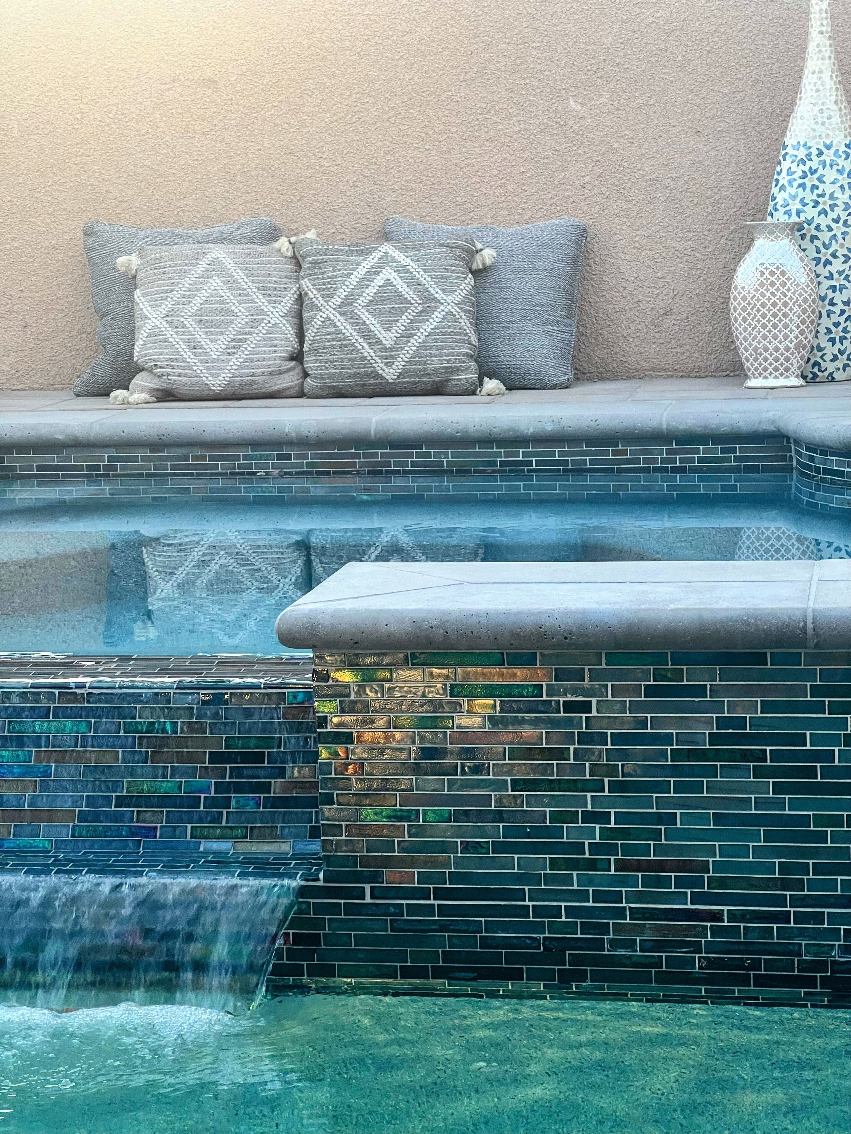 A pool area with a tiled wall, a small waterfall feature, and a seating area with cushions.